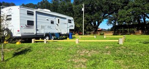 A recreational vehicle (RV) parked in a grassy field with a wooden fence and trees in the background. - Serene 1-bedroom, 1-bathroom, 5th wheel with AC, farms next-door near Lucedale. (Lucedale)