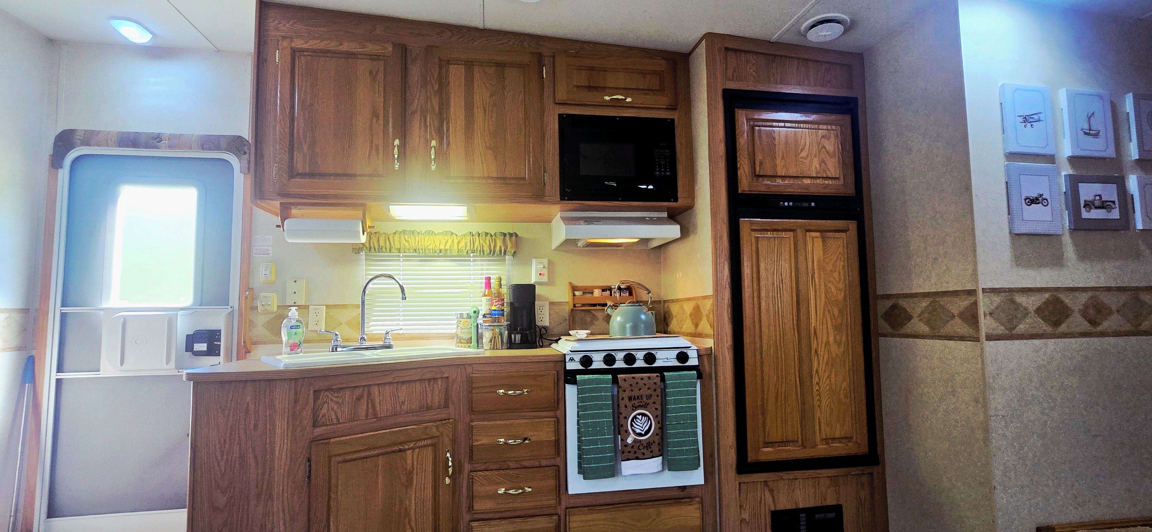 A compact RV kitchen with wooden cabinets, a stove, a microwave, and a sink.