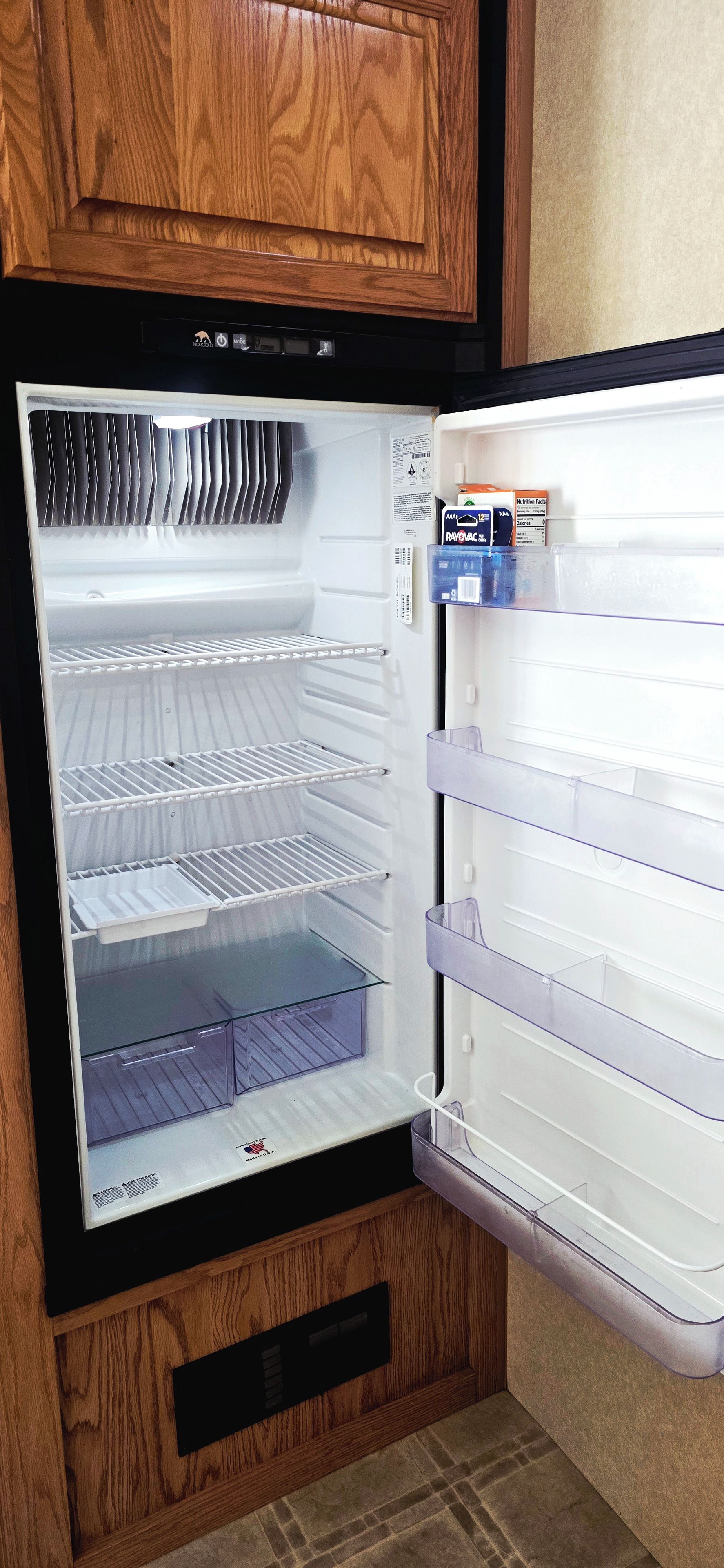 A refrigerator with multiple shelves and a freezer compartment, with a wooden cabinet above it.