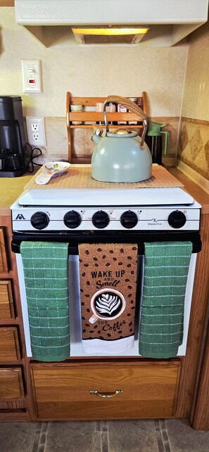 A kitchen with a stove, a kettle, and two green towels with coffee-related designs. - Serene 1-bedroom, 1-bathroom, 5th wheel with AC, farms next-door near Lucedale. (Lucedale)