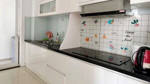 A modern kitchen with white cabinets, a black countertop, and a backsplash with food-related illustrations. - EMERALD CELADON CITY 2PN2WC (Thanh pho Chi Minh)
