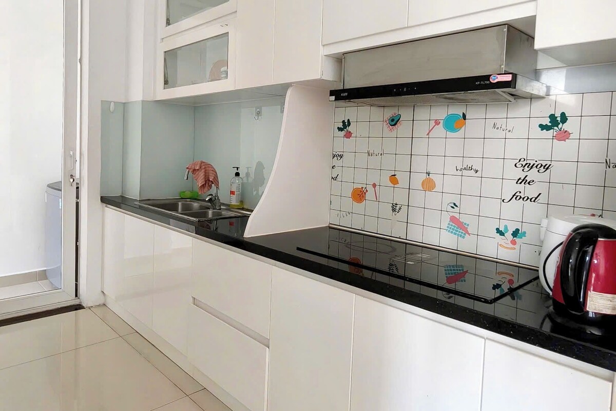 A modern kitchen with white cabinets, a black countertop, and a backsplash with food-related illustrations.