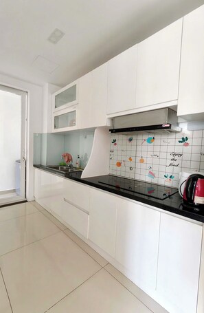 A modern kitchen with white cabinets, a black countertop, and a backsplash with food-related illustrations. - EMERALD CELADON CITY 2PN2WC (Thanh pho Chi Minh)