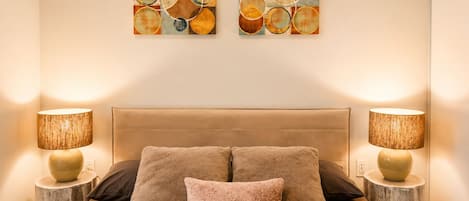 Un dormitorio con una cama grande, dos lámparas de pared y dos cuadros abstractos.