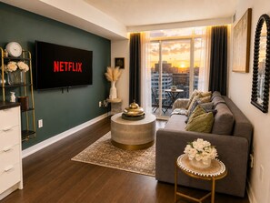 Ein modernes Wohnzimmer mit einem Flachbildfernseher, einer Couch, einem Couchtisch und Blick auf die Stadt durch große Fenster.