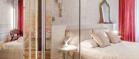 A bedroom with a large bed, a bedside table, a mirror, and a red curtain.