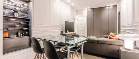 Un moderno comedor con mesa y sillas de vidrio, una estantería empotrada para vinos y un sofá con una mesita auxiliar.