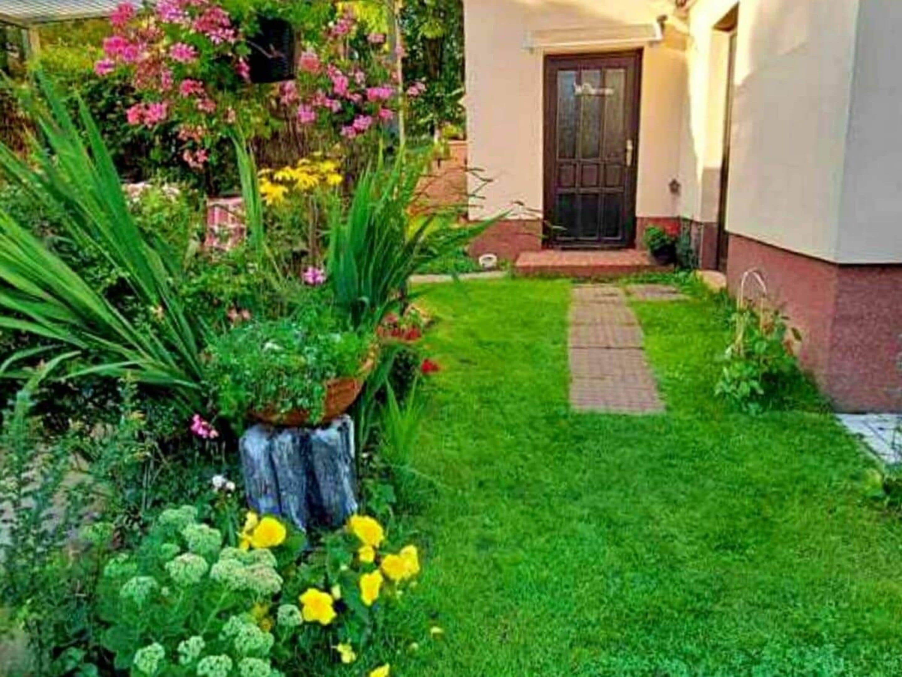 A well-maintained garden with a variety of flowers and plants, a paved pathway leading to a door, and a small water feature.