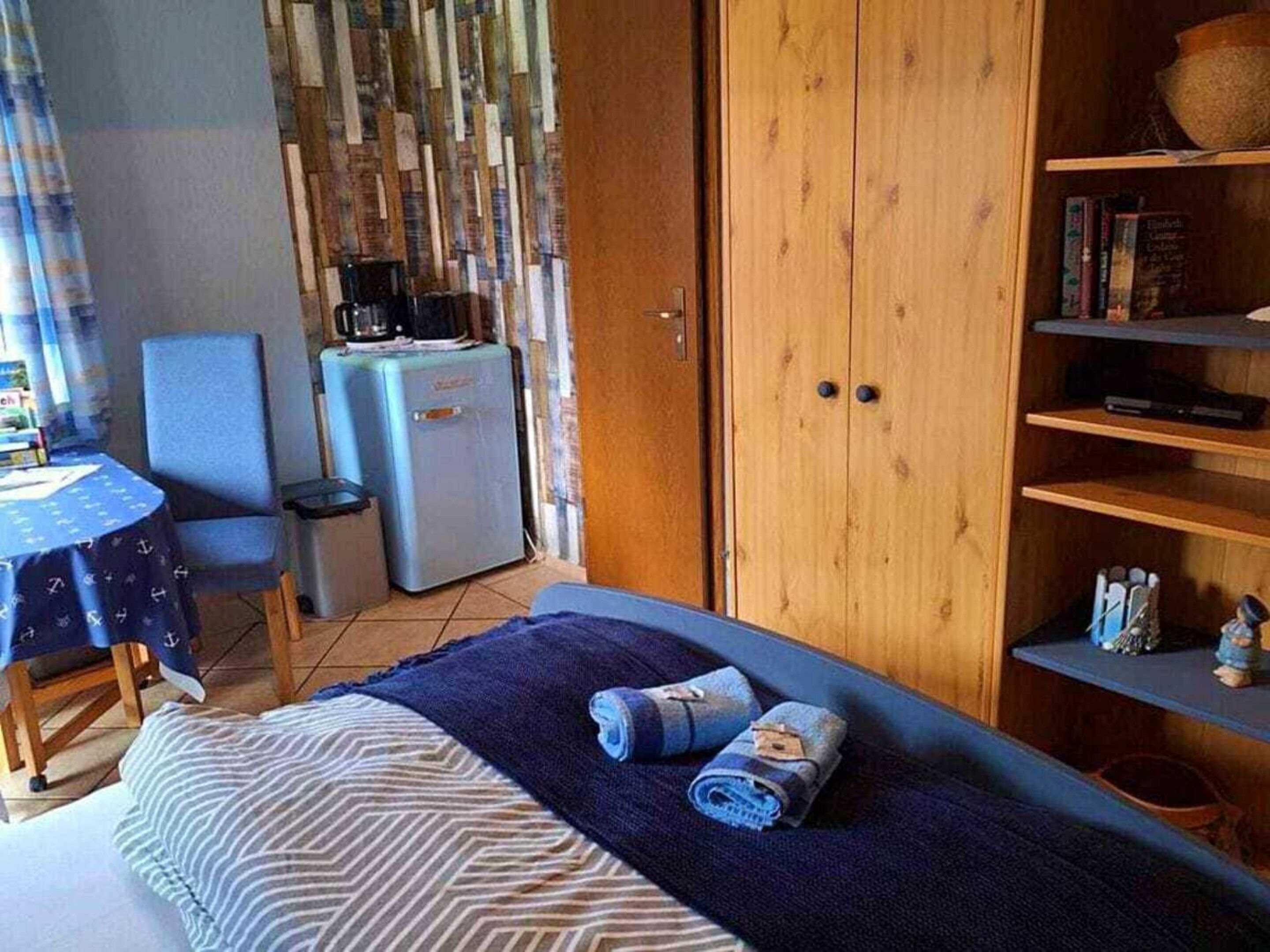 A bedroom with a bed, a desk, a chair, a small refrigerator, and a wardrobe.
