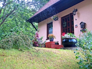 A house with a red brick exterior, a thatched roof, and a garden with various plants and flowers. - Vacation at Umlauf (Heringsdorf)
