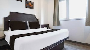 Una habitación de hotel con una cama grande, cabecero, dos cuadros en la pared, una ventana con cortinas y suelo de madera.