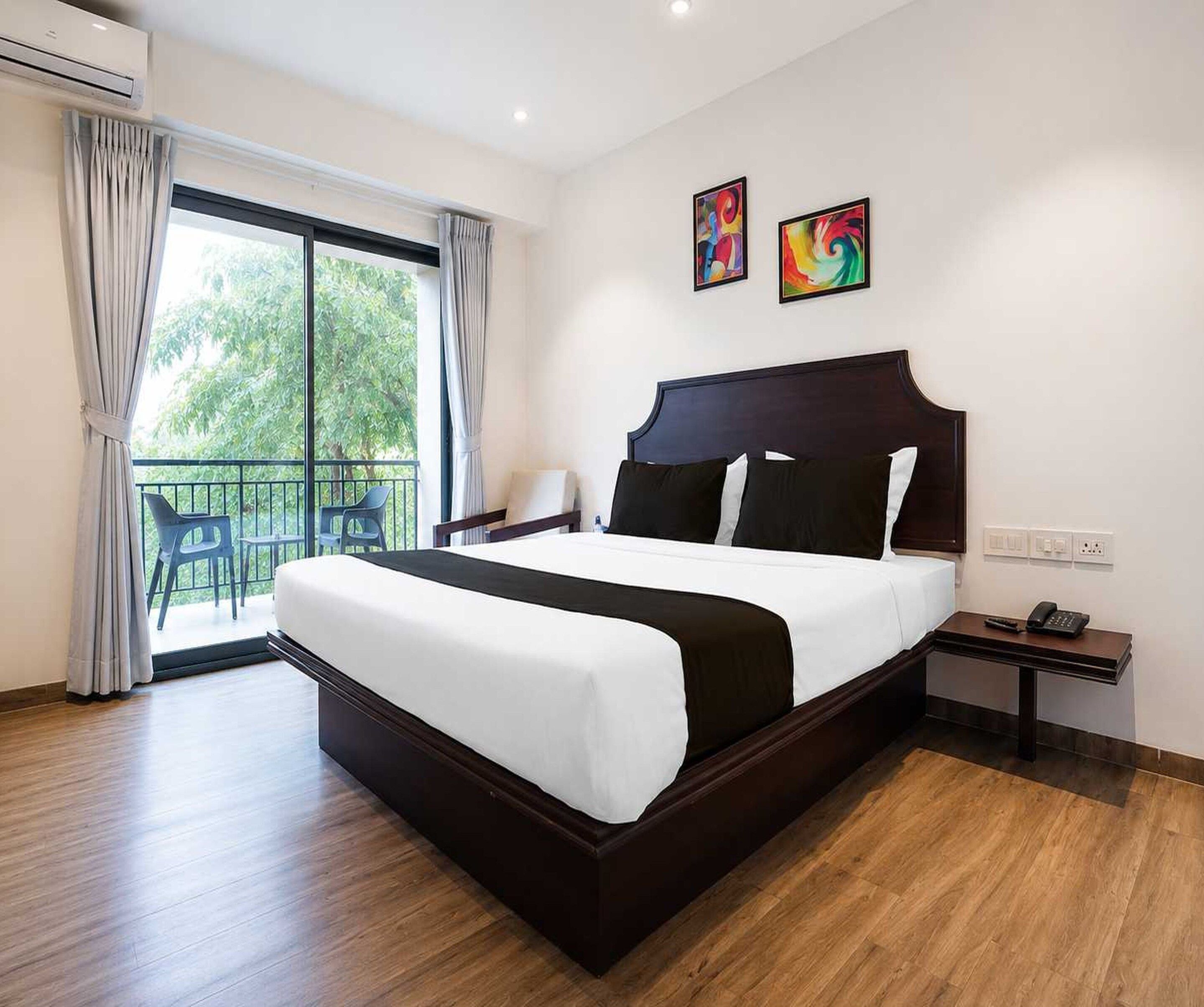 A hotel room with a large bed, a balcony with chairs, and two abstract paintings on the wall.