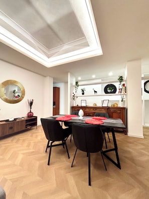 Zona pranzo con soffitto alto e lucernario, pavimento in legno a spina di pesce e tavolo da pranzo nero moderno con sedie.