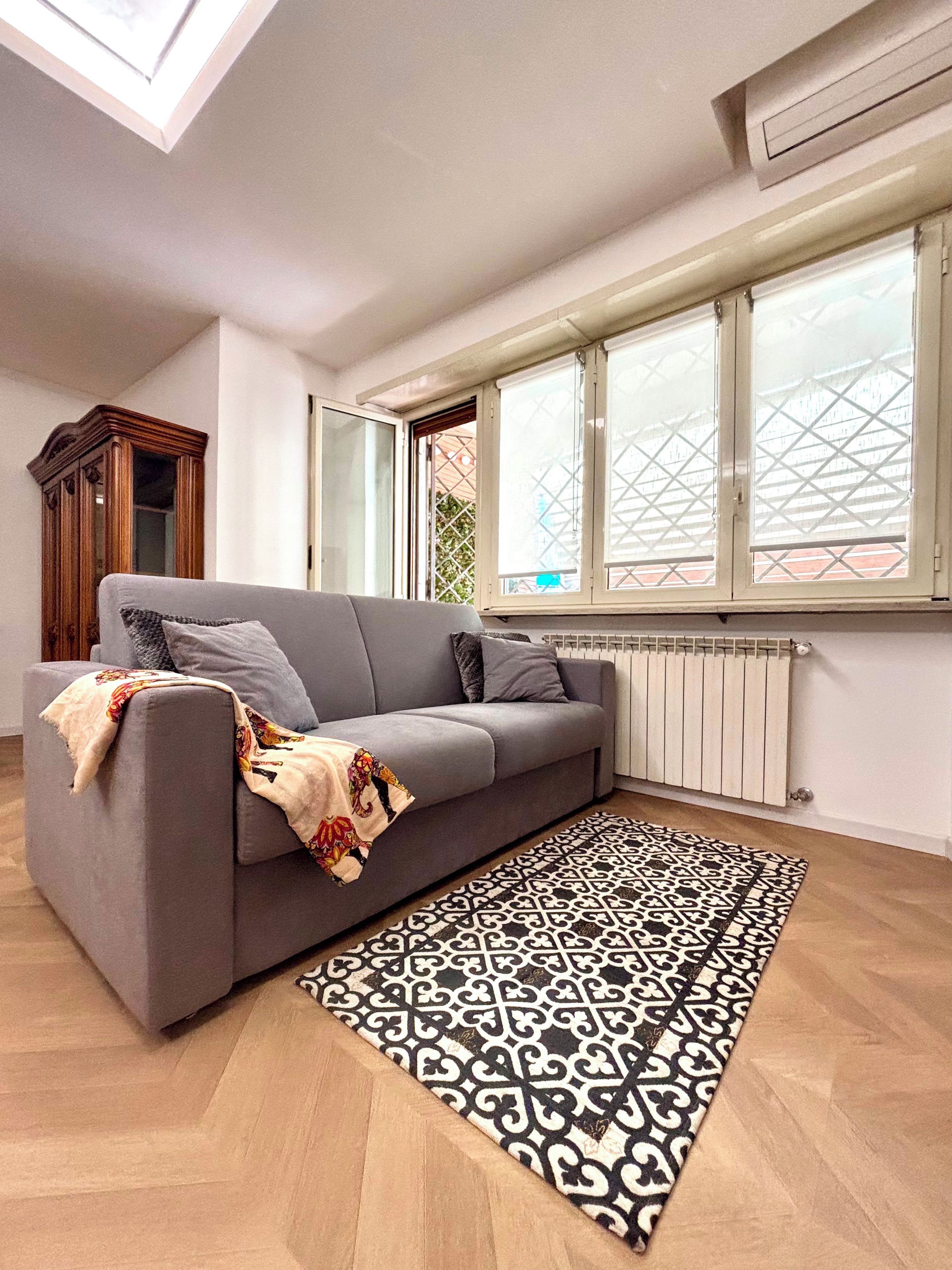 Ein modernes Wohnzimmer mit einem grauen Sofa, einem gemusterten Teppich und einem Fenster mit Blick.