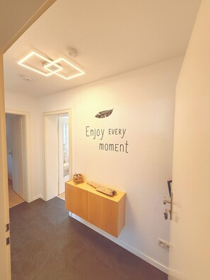 En hall med ett träskåp, en vägg dekorerad med fjädrar och text, och en taklampa.