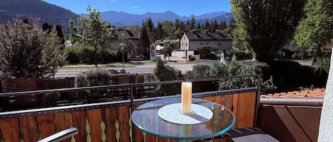 A balcony with a glass table and chairs, overlooking a mountainous landscape.