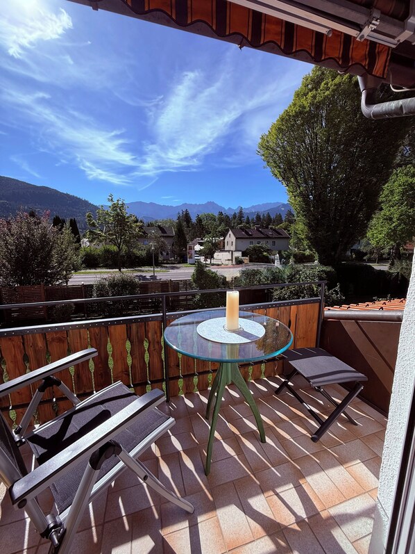 Un balcon avec une table et des chaises en verre, donnant sur un paysage montagneux.