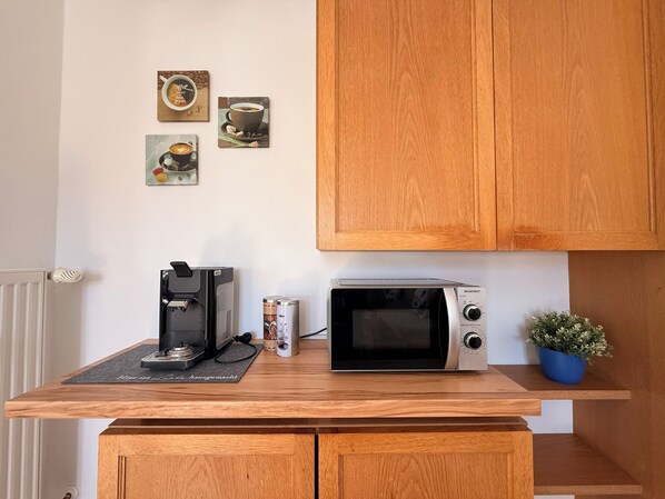 Una cocina con cafetera, microondas y un cuadro con motivos de café.