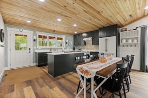 Una cocina moderna con una isla central, armarios oscuros y una zona de comedor con mesa y sillas.