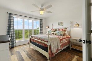 Un dormitorio con cama, ventilador de techo, mesita de noche, lámpara y vistas al exterior.