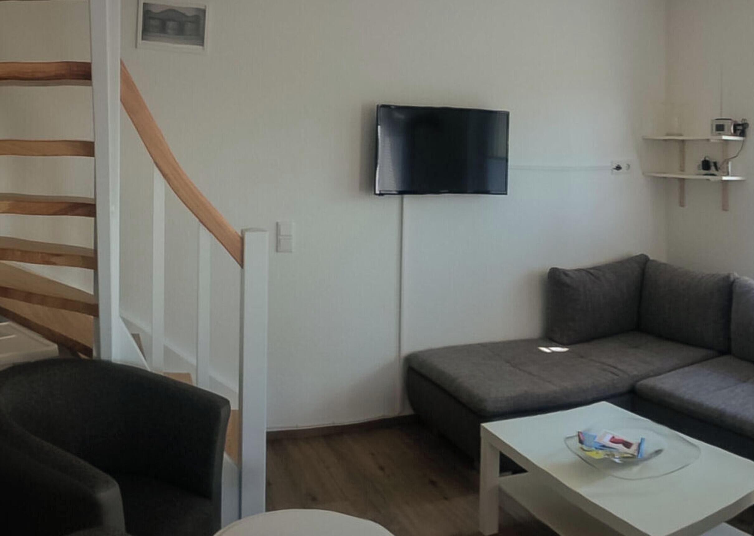 A living room with a sofa, a television mounted on the wall, and a staircase with wooden steps.