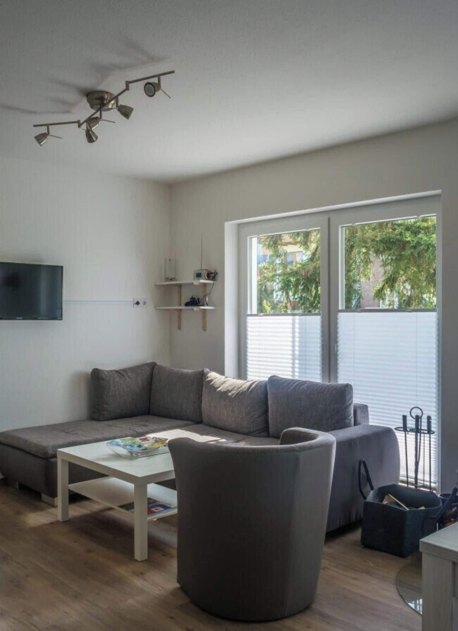 A modern living room with a sectional sofa, a round ottoman, and a flat-screen TV.