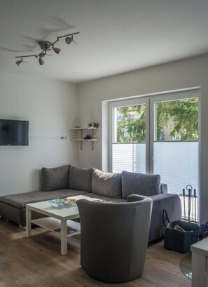A modern living room with a sectional sofa, a round ottoman, and a flat-screen TV. - Holiday Home Oasis in the Muritz Lake Park (Röbel/Müritz)