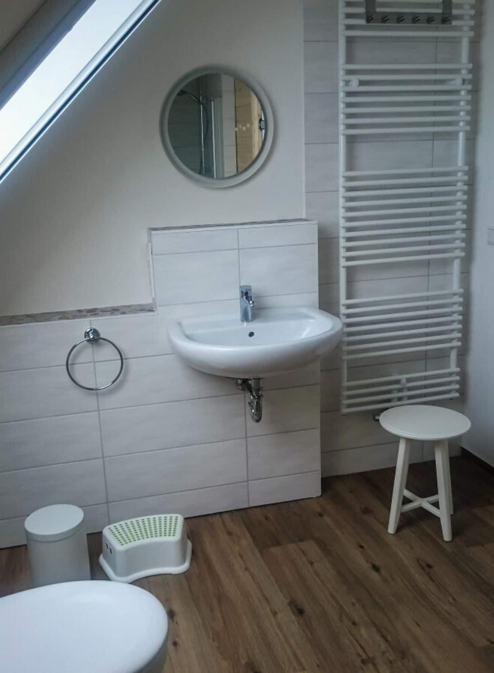 Een moderne badkamer met dakraam, een ronde spiegel, een wastafel, toilet en een klein krukje.