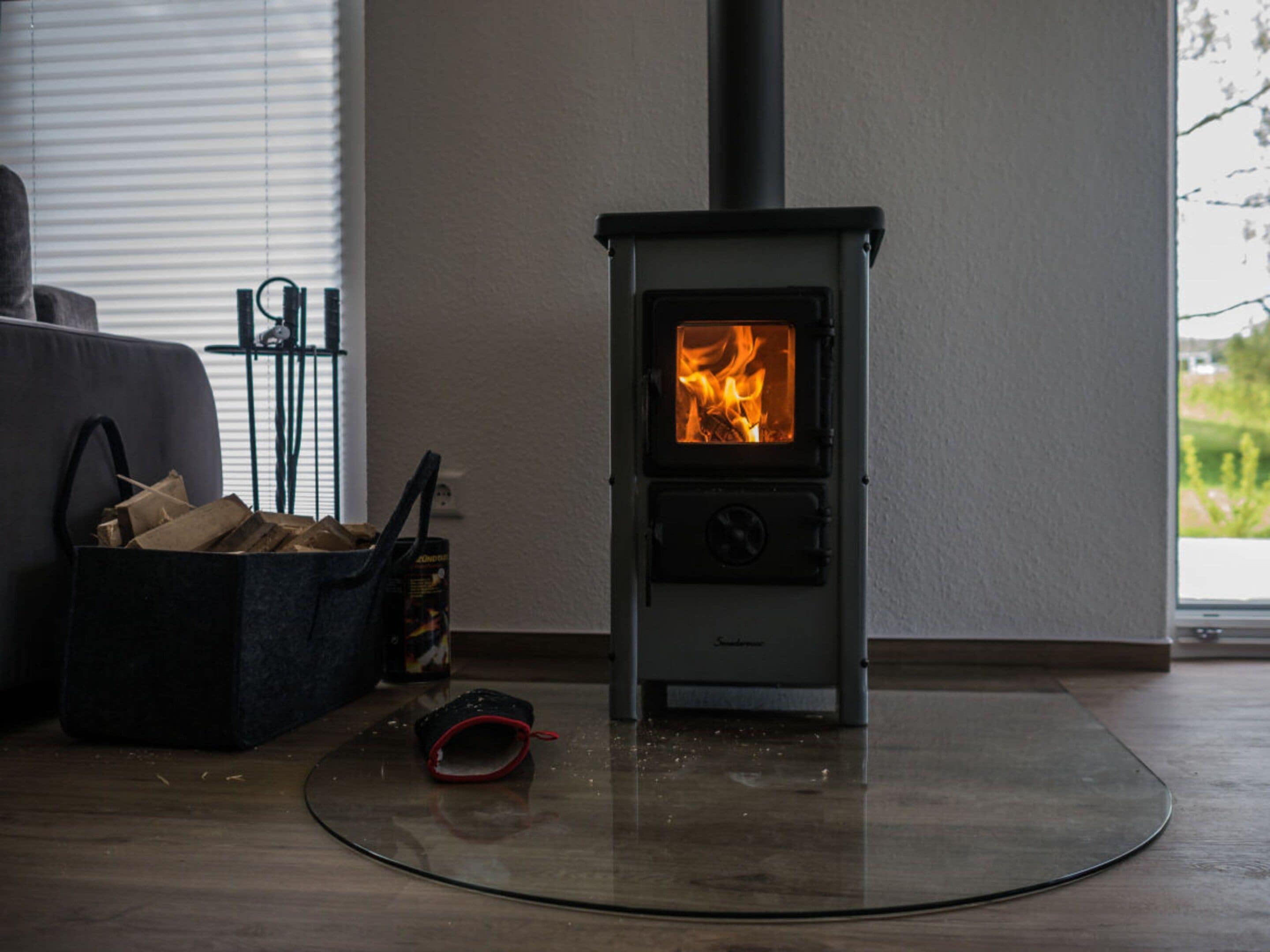En brændeovn i et rum med et vindue, en sofa og en pose brænde.