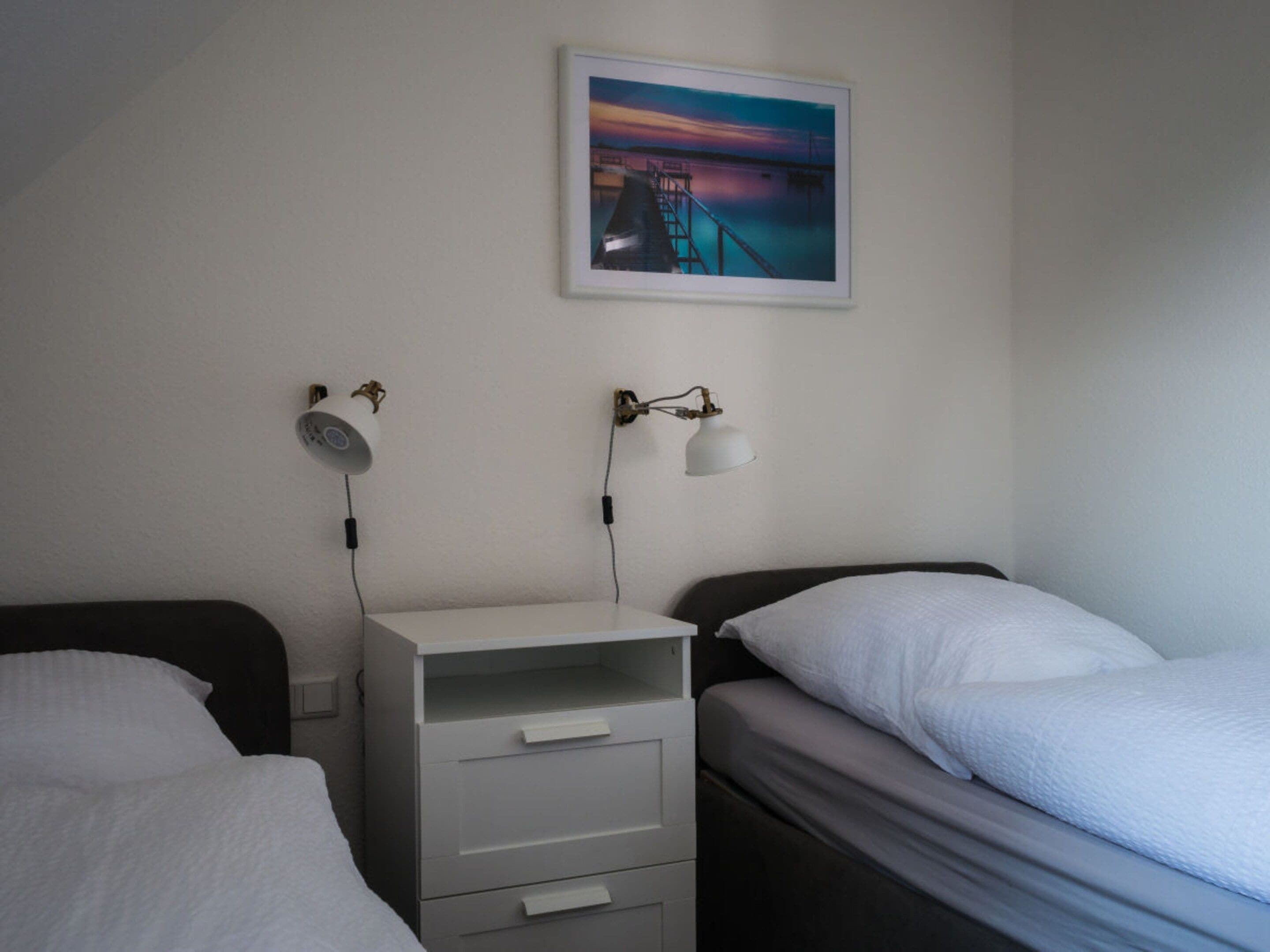 Een slaapkamer met twee bedden, een nachtkastje, een bureau en een wandlamp.