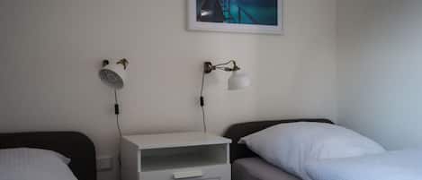 Une chambre avec deux lits, une table de chevet, un bureau et une lampe fixée au mur.