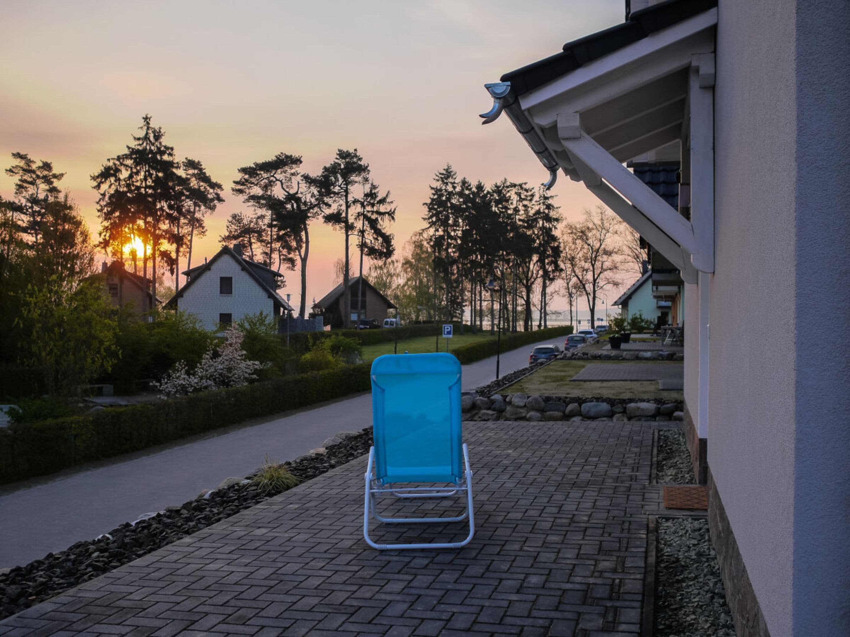 A paved outdoor area with a blue lounge chair, a pathway, and houses in the background.