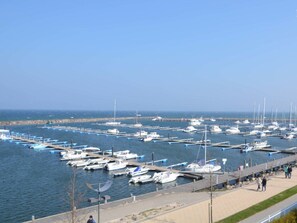 Ein Yachthafen mit vielen angestoßenen Booten, einer Uferpromenade und wolkenlosem Himmel.
