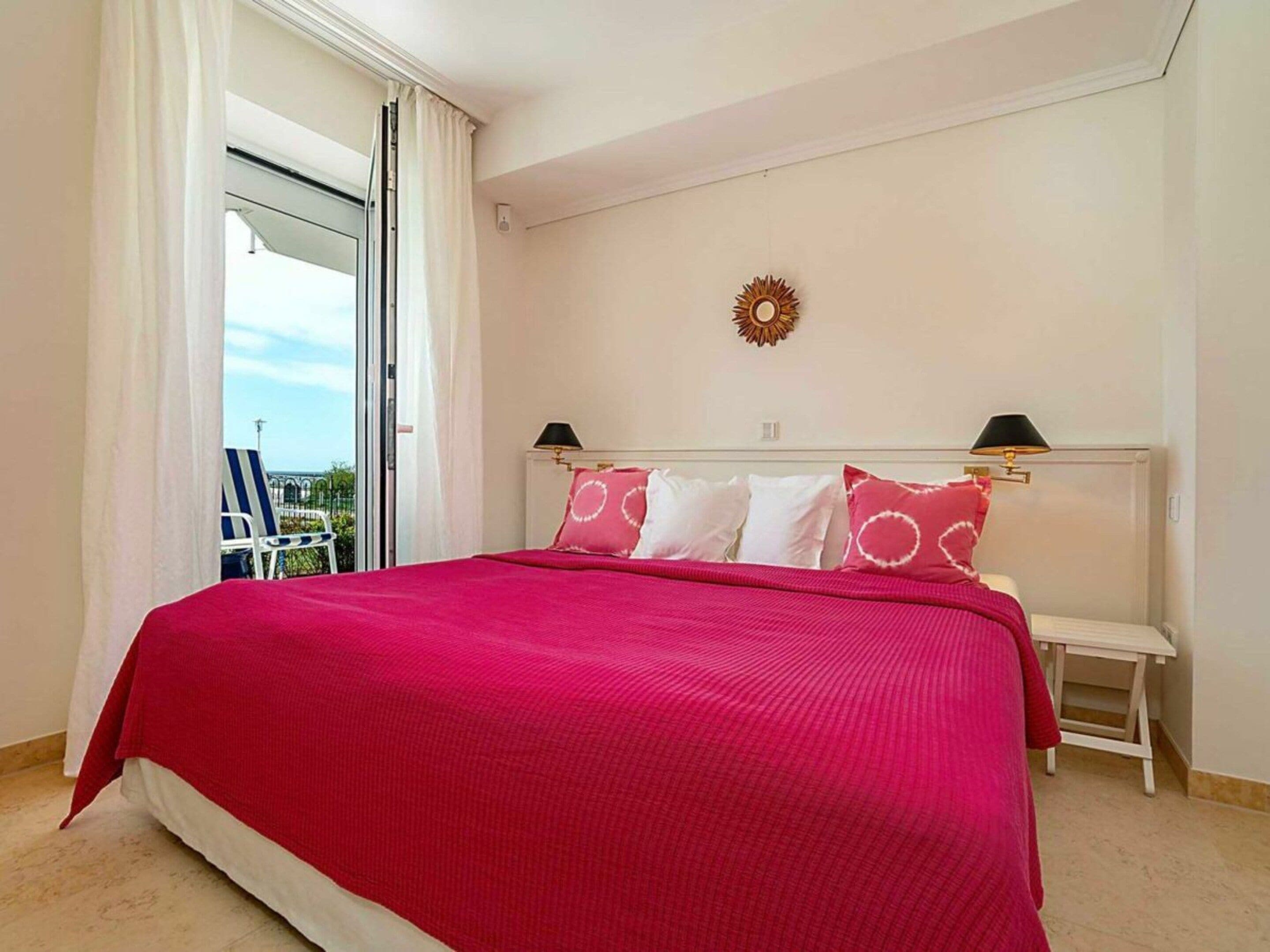 A bedroom with a large bed, a nightstand, a wall-mounted lamp, and a view through an open door.