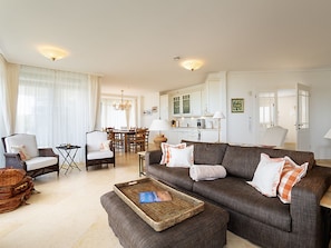 Ein geräumiges Wohnzimmer mit Sofa, Sesseln, einem Esstisch und einer Küche im Hintergrund.