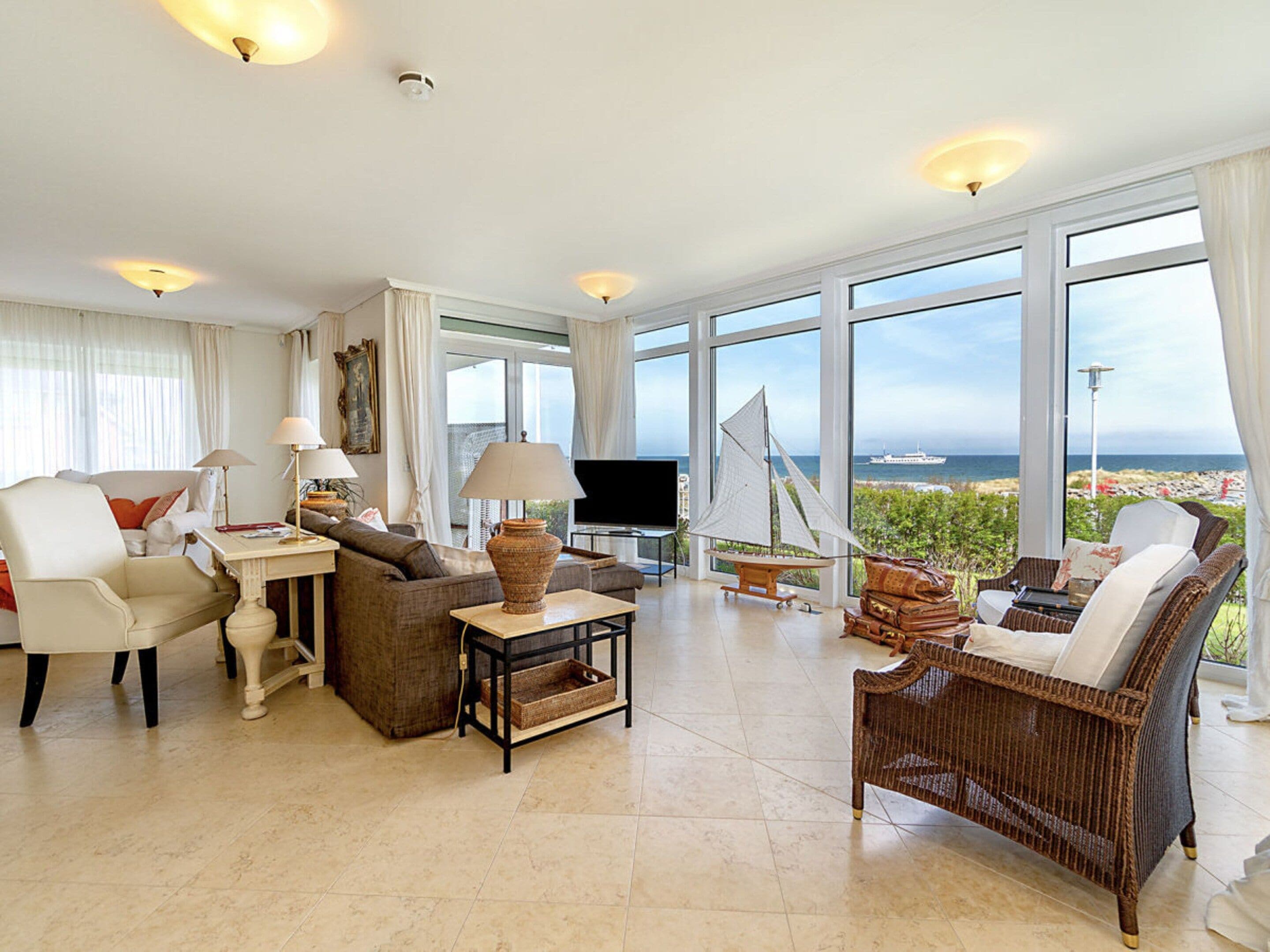 A spacious living room with a large window offering a view of the sea, a television, and comfortable seating.