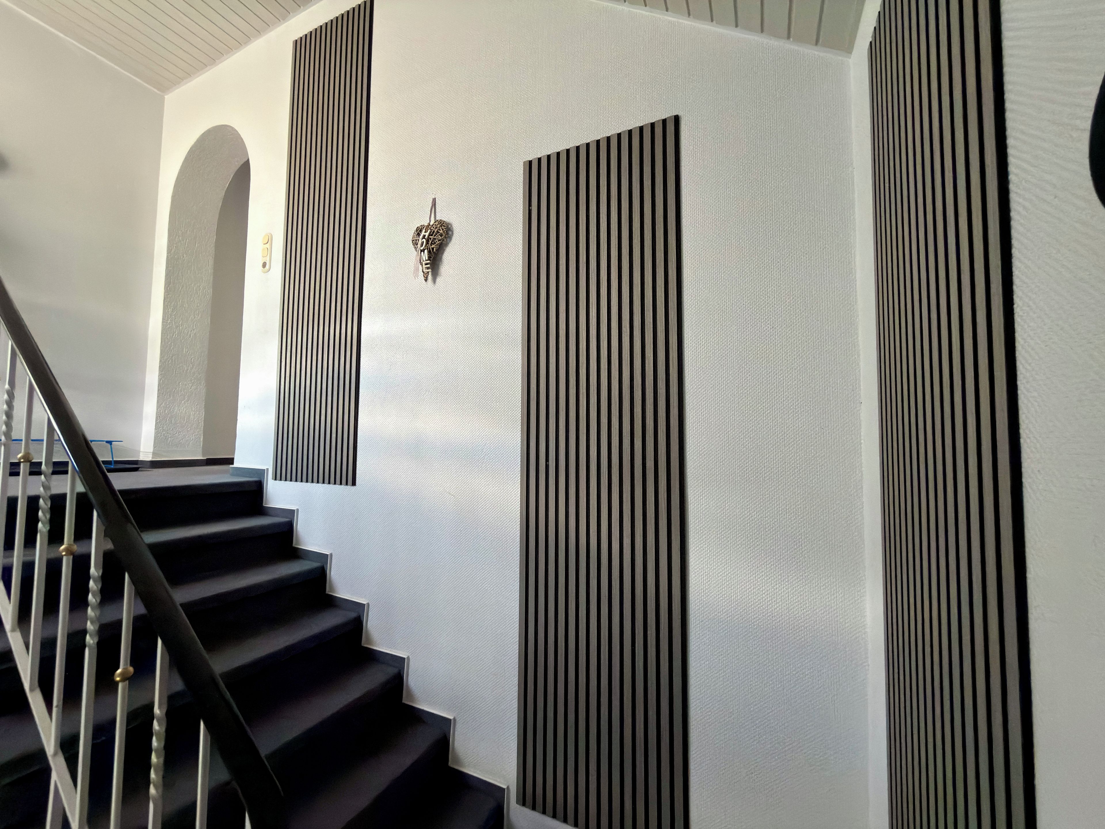Uma escadaria com design moderno, com corrimão preto e paredes brancas com listras verticais pretas.
