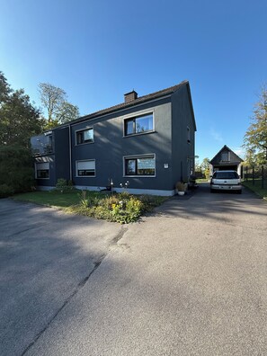 A two-story residential building with a garage, a driveway, and a small garden with flowers.