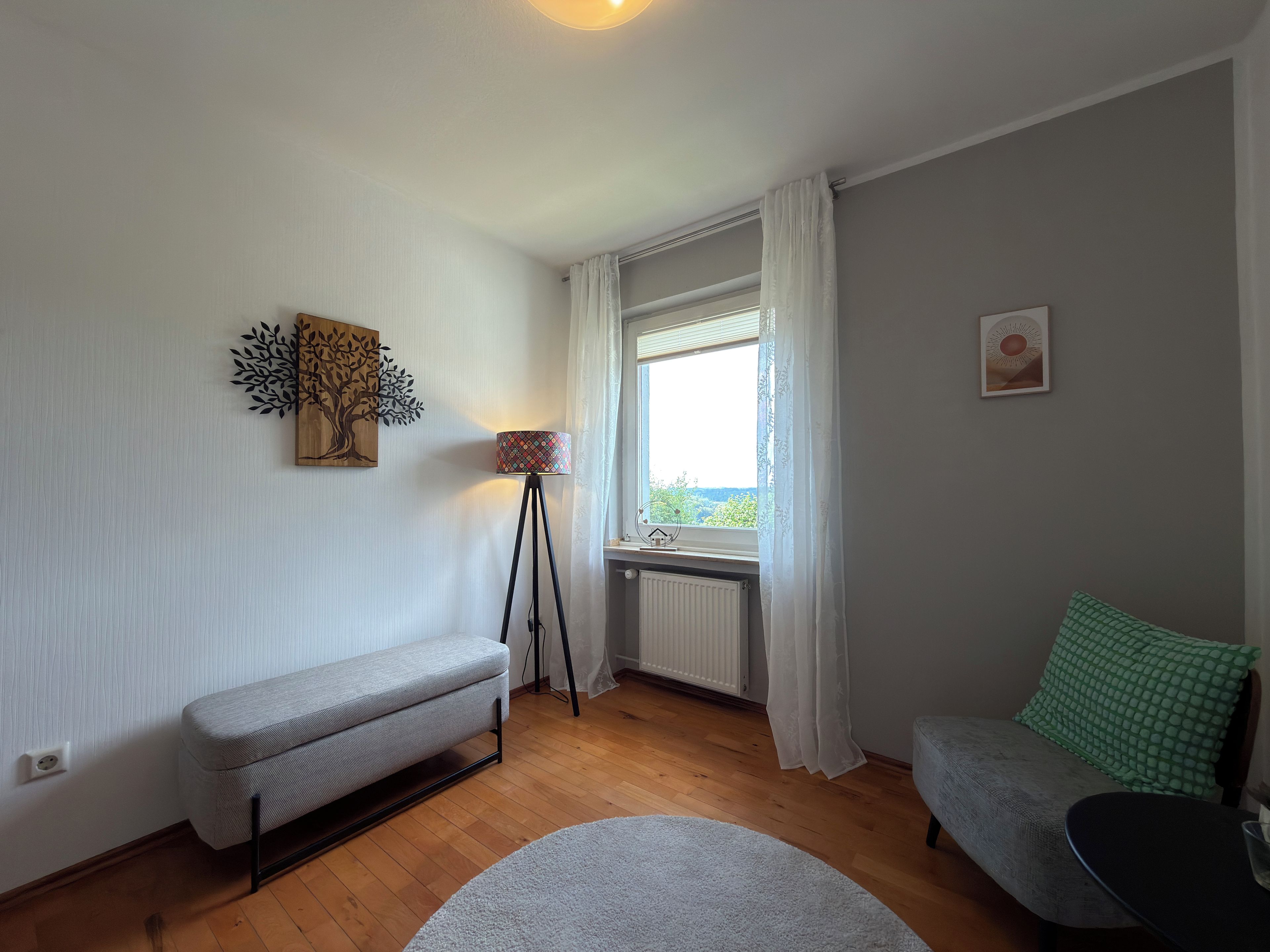 Quarto com um banco, luminária de chão, sofá e vista pela janela.
