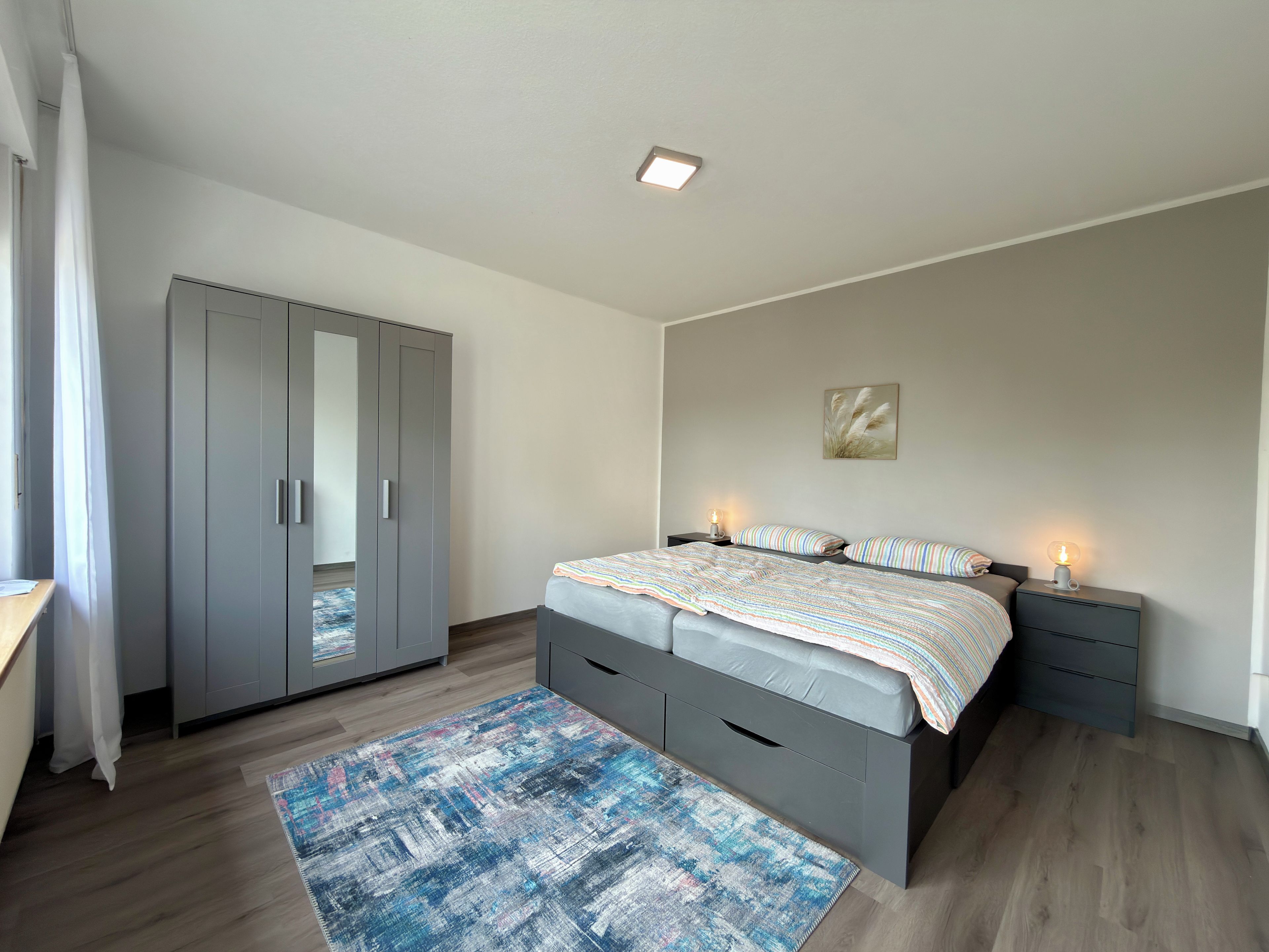 Ein Schlafzimmer mit einem Bett, Nachttischen, einem Kleiderschrank und einem Teppich.