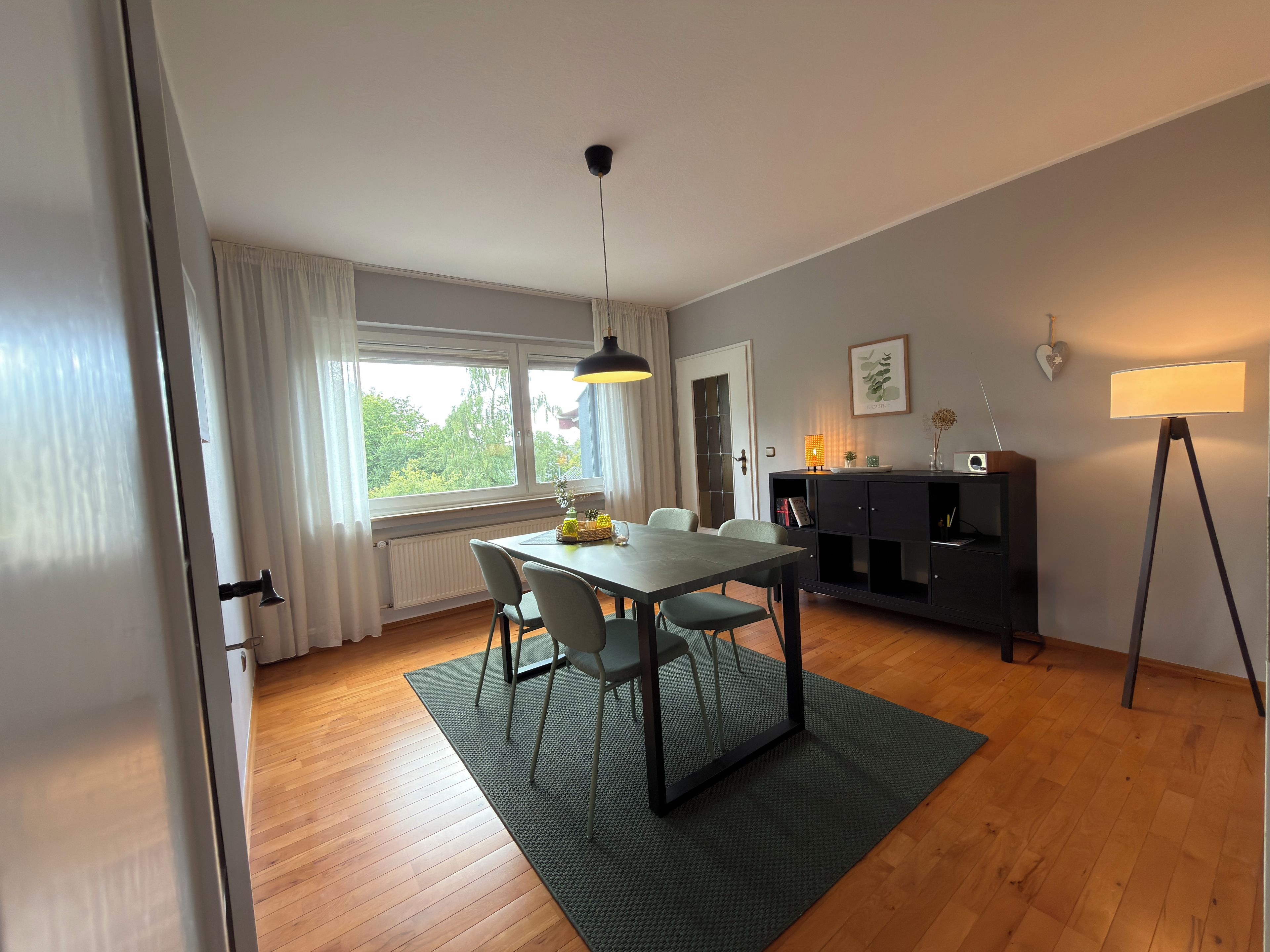 Ein moderner Essbereich mit Tisch, Stühlen, einer Stehlampe und Blick durch ein Fenster.