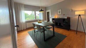 Uma sala de jantar moderna com uma mesa, cadeiras, um abajur e vista pela janela.