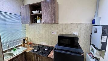 A compact kitchen with a gas stove, a microwave, wooden cabinets, and a small countertop.