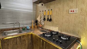 A kitchen with a gas stove, a sink, wooden cabinets, and a window with blinds.