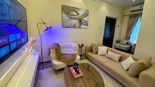 A modern living room with a flat-screen TV, a sofa, a coffee table, and a painting on the wall. - Haven 21;  Luxury 1-Bedroom Serviced Apartment in Ajah (Close)