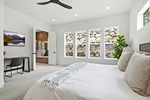 Ein Schlafzimmer mit einem großen Bett, einem Schreibtisch und Blick auf eine felsige Landschaft durch die Fenster.