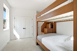 En våningssäng med en träram och en inbyggd hylla, en vit dörr och ett fönster som släpper in dagsljus.