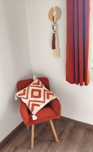 A corner room with a red chair, a patterned throw pillow, a wall-mounted tassel, and a red curtain.
