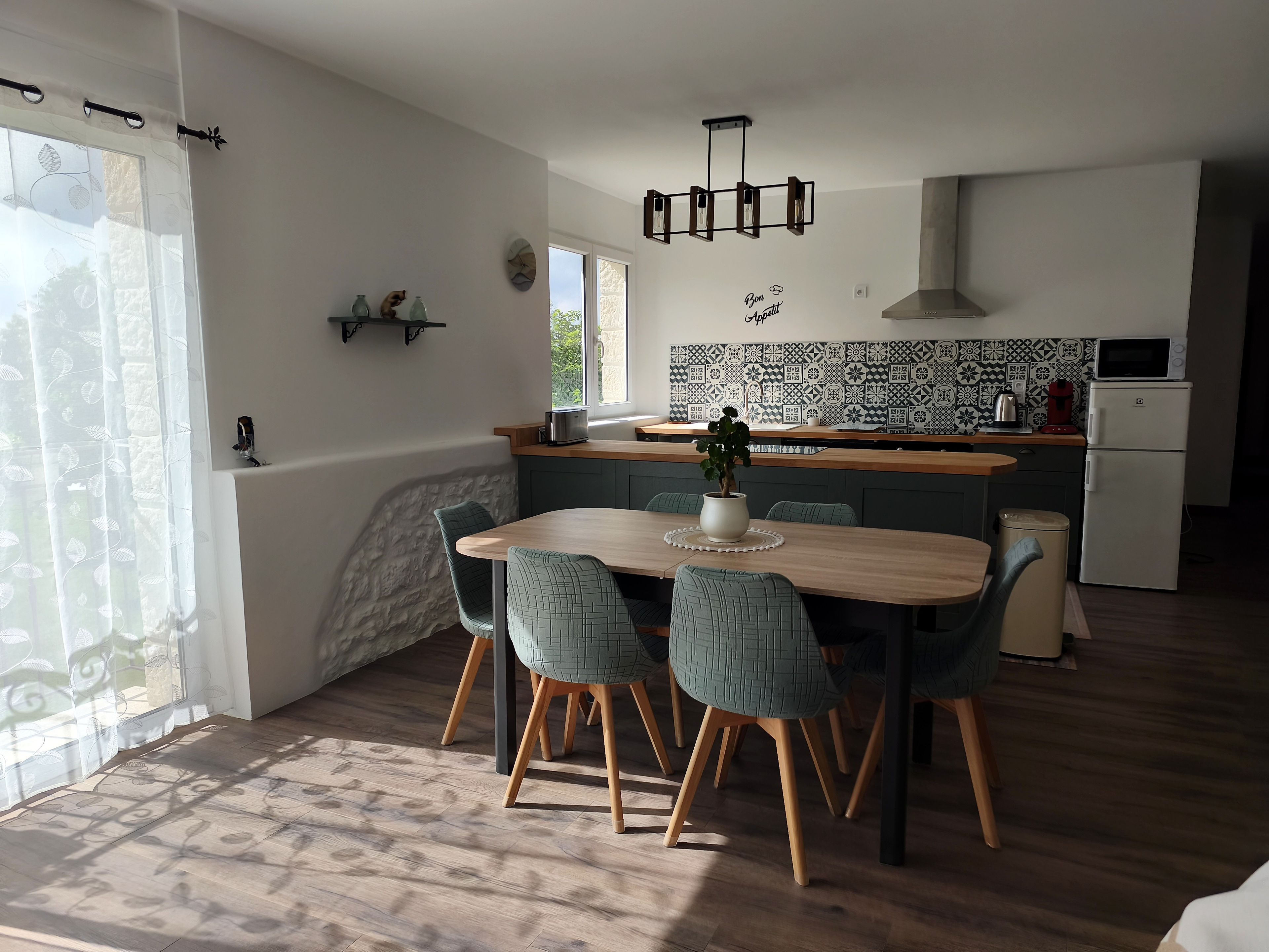 Une cuisine moderne avec un coin repas, comprenant une table en bois, des chaises vertes et une plante en pot.