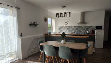 A modern kitchen with a dining area, featuring a wooden table, green chairs, and a potted plant.